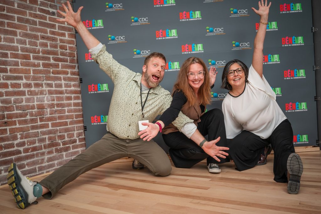 Trois invité·es prennent la pose devant le mur de photos BÉNÉVAL